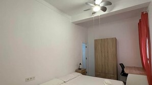 Une chambre avec deux lits, un ventilateur de plafond, une armoire en bois et un rideau rouge.