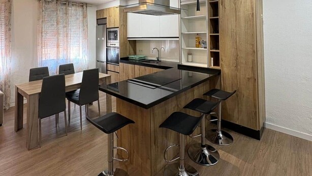 Une cuisine moderne dotée d’un îlot central, de tabourets de bar, d’une table à manger avec des chaises et d’une bibliothèque intégrée.