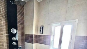 A shower area with a handheld showerhead, a wall-mounted control panel, and a glass door. - House in La Corredera (Córdoba)