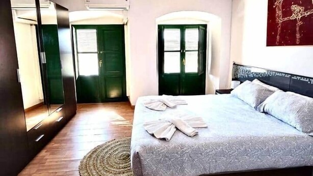 A bedroom with a bed, wooden beams, a green door, and a mirror. - House in La Corredera (Córdoba)