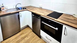 A compact kitchen with white cabinets, a wooden countertop, stainless steel appliances, and a black TV mounted on the wall. - House in La Corredera (Córdoba)