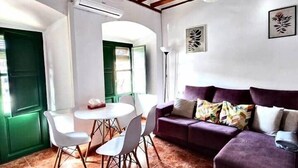 A living room with a purple sofa, a dining table with chairs, and a tiled floor. - House in La Corredera (Córdoba)