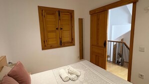 Une chambre à coucher avec un lit, des oreillers, une armoire en bois et une porte donnant sur un escalier.