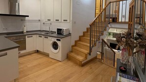 Une cuisine moderne dotée d’appareils électroménagers intégrés, d’un lave-linge et d’un escalier en bois menant à une chambre située en mezzanine.