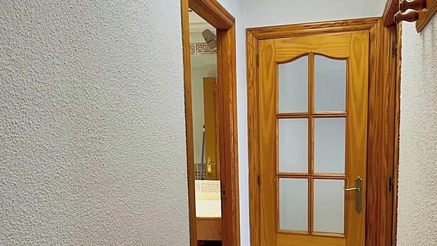 A wooden door with a frosted glass panel, a mirror above it, and a white textured wall. - Apartment in Casco Historico (Córdoba)