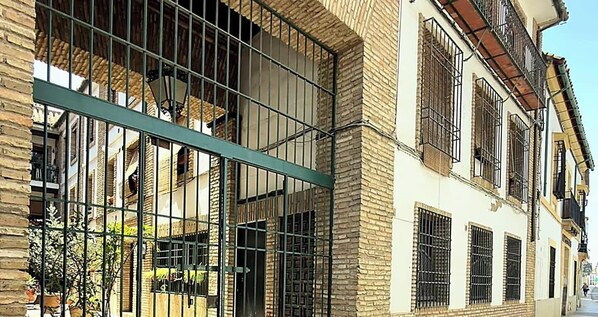 A building with multiple windows, some with metal bars, and a green metal structure in front. - Apartment in Casco Historico (Córdoba)