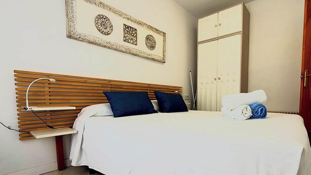 A bedroom with a bed, a wooden headboard, a wall-mounted picture, a wardrobe, and a door. - Apartment in Casco Historico (Córdoba)