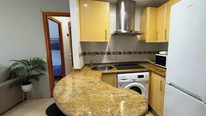 A compact kitchen with granite countertops, a built-in microwave, a stainless steel range hood, a washing machine, and a refrigerator. - Apartment in Casco Historico (Córdoba)