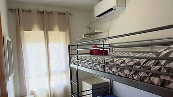 Une chambre avec un lit superposé, un ventilateur de plafond, une petite table et une fenêtre avec des rideaux.