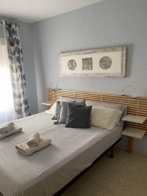 A neatly made bed with pillows and rolled towels, a wooden headboard, and a wall-mounted artwork. - Apartment in Casco Historico (Córdoba)