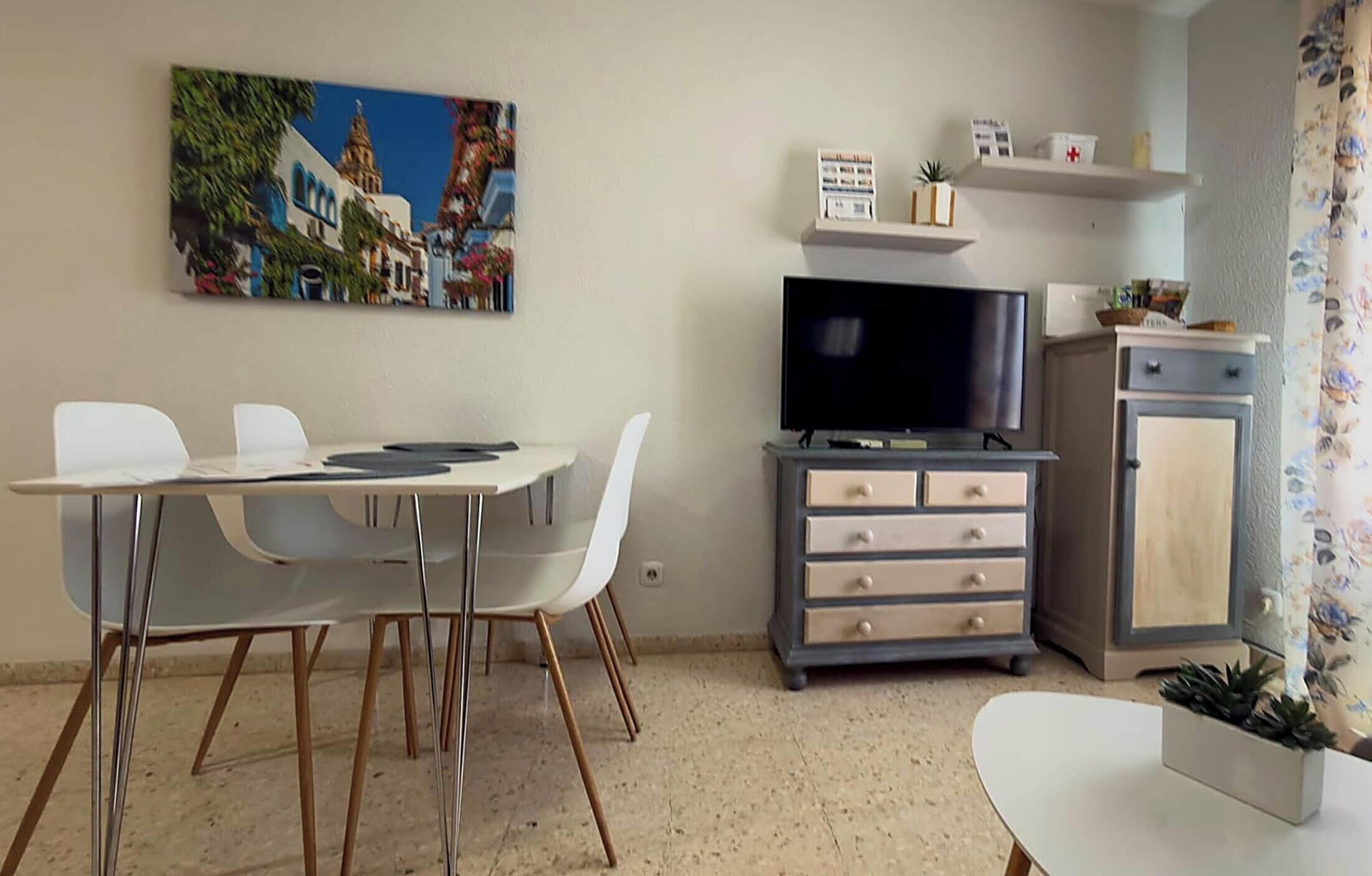 Un espace de vie compact comprenant une table à manger, des chaises, un téléviseur à écran plat, un meuble et une petite plante.