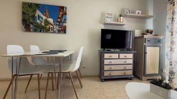 Un espace de vie compact comprenant une table à manger, des chaises, un téléviseur à écran plat, un meuble et une petite plante.