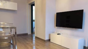 Ein modernes Wohnzimmer mit Flachbildfernseher an der Wand, einer weißen Unterhaltungsanlage und einem Glastisch.