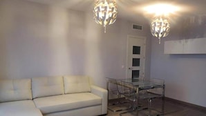 Ein Wohnzimmer mit einem weißen Sofa, einem Glastisch mit Stühlen und zwei Kronleuchtern.