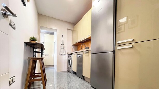 Een moderne keuken met een roestvrijstalen koelkast, een wasmachine en een houten stoel.