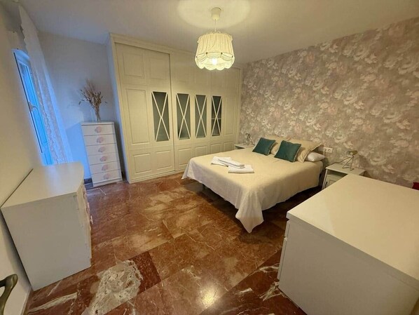 Une chambre à coucher comprenant un lit, une table de chevet, une commode et une fenêtre avec des rideaux.