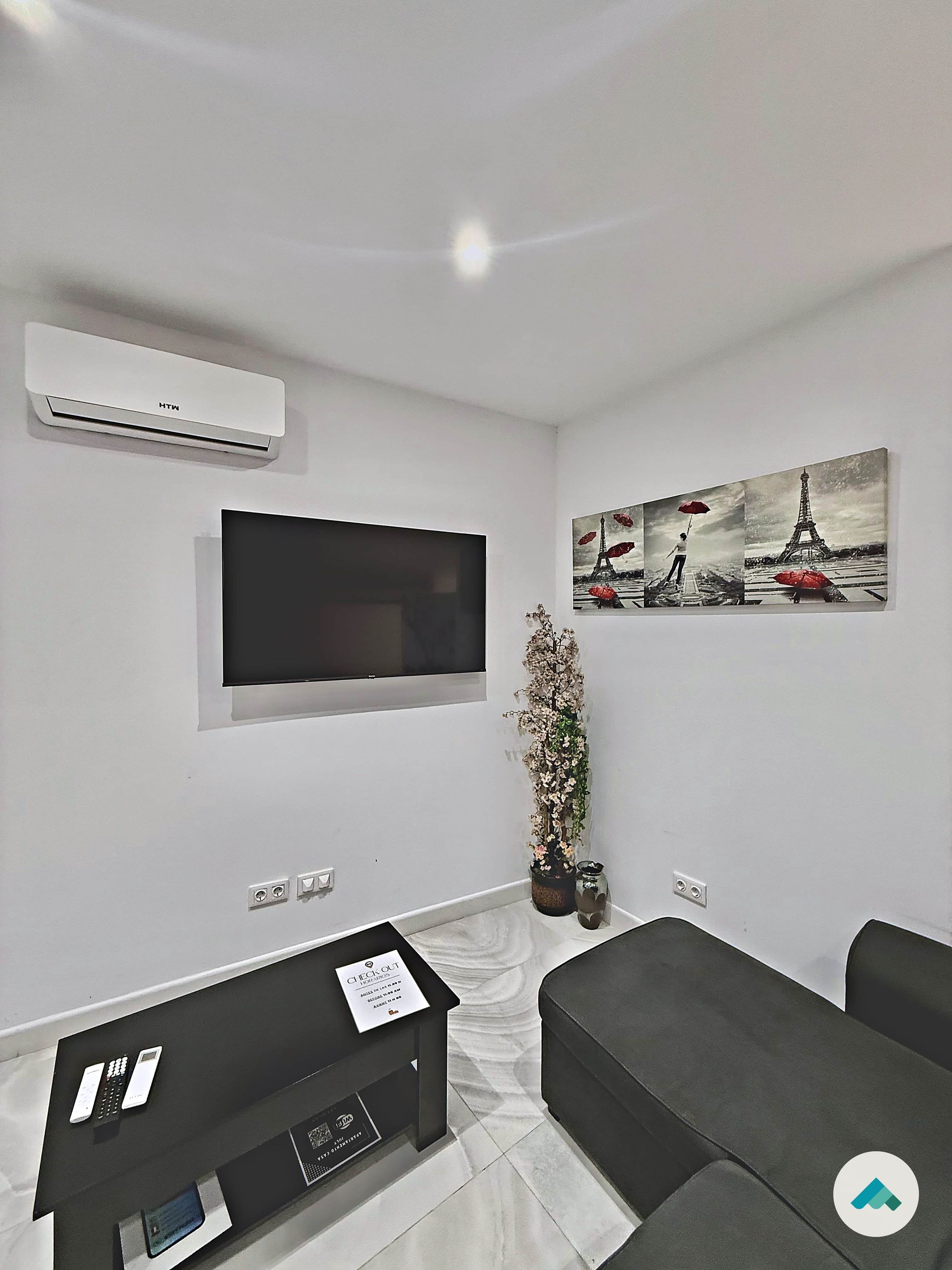 Uma sala de estar moderna com televisão de tela plana, um sofá preto, uma mesa de jantar e uma pintura da Torre Eiffel.