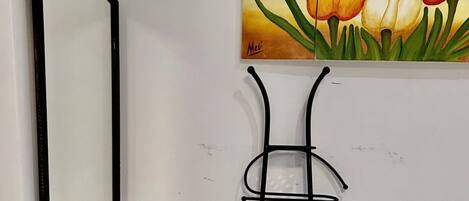 A room with a black metal shelf unit, a mirror, and a painting of tulips on the wall.