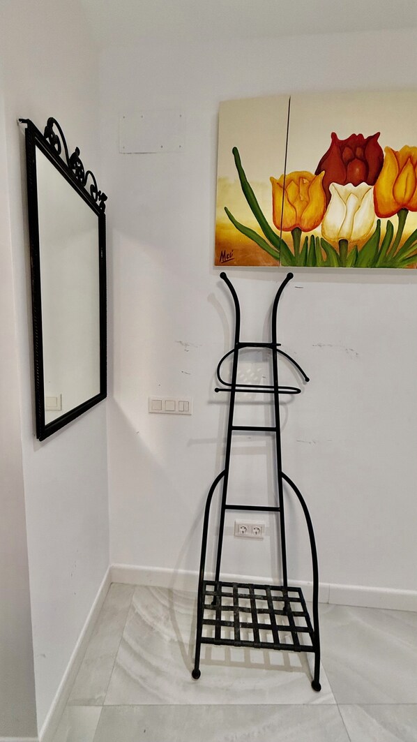Una habitació amb un prestatge metàllic negre, un mirall i un quadre de tulipes a la paret.