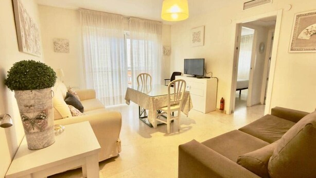 Ein Wohnzimmer mit einer Couch, einem Esstisch mit Stühlen, einem Fernseher und einer Topfpflanze.