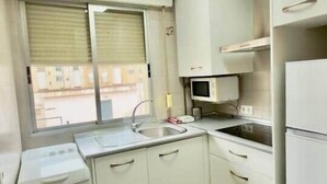 Eine kleine Küche mit weißen Schränken, einer Mikrowelle, einem Spülbecken und einem kleinen Kühlschrank.