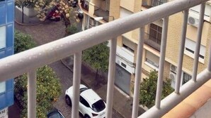 Ein Wohngebiet mit mehrstöckigen Gebäuden, ein weißes Auto im Vordergrund und einem Balkongeländer.
