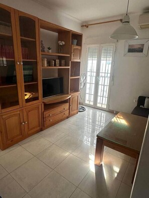 A living room with a wooden cabinet, a flat-screen TV, a dining table, and a sliding glass door. - El Indiano Apartment (Córdoba)