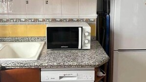 Kompakti keittiö, jossa on puukaapit, mikroaaltouuni, astianpesukone ja jääkaappi.