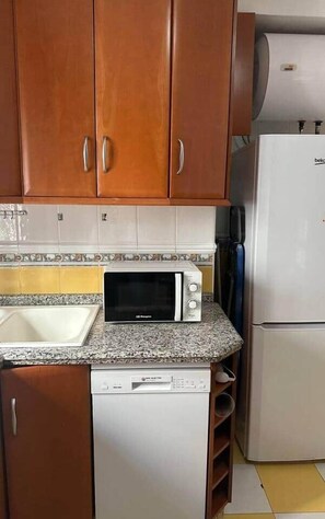 Une cuisine de taille réduite, dotée de meubles en bois, d’un four à micro-ondes, d’un lave-vaisselle et d’un réfrigérateur.
