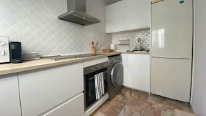A compact kitchen with white cabinetry, a built-in oven, a washing machine, and a refrigerator. - Quédate cerca del casco antiguo (Córdoba)