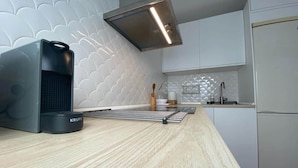 A modern kitchen with a sleek black coffee maker, a stainless steel range hood, and a white refrigerator. - Quédate cerca del casco antiguo (Córdoba)