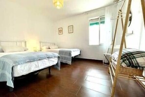 A bedroom with two beds, a wooden floor, a window with curtains, and a chair. - Casa Paula in Córdoba (Córdoba)