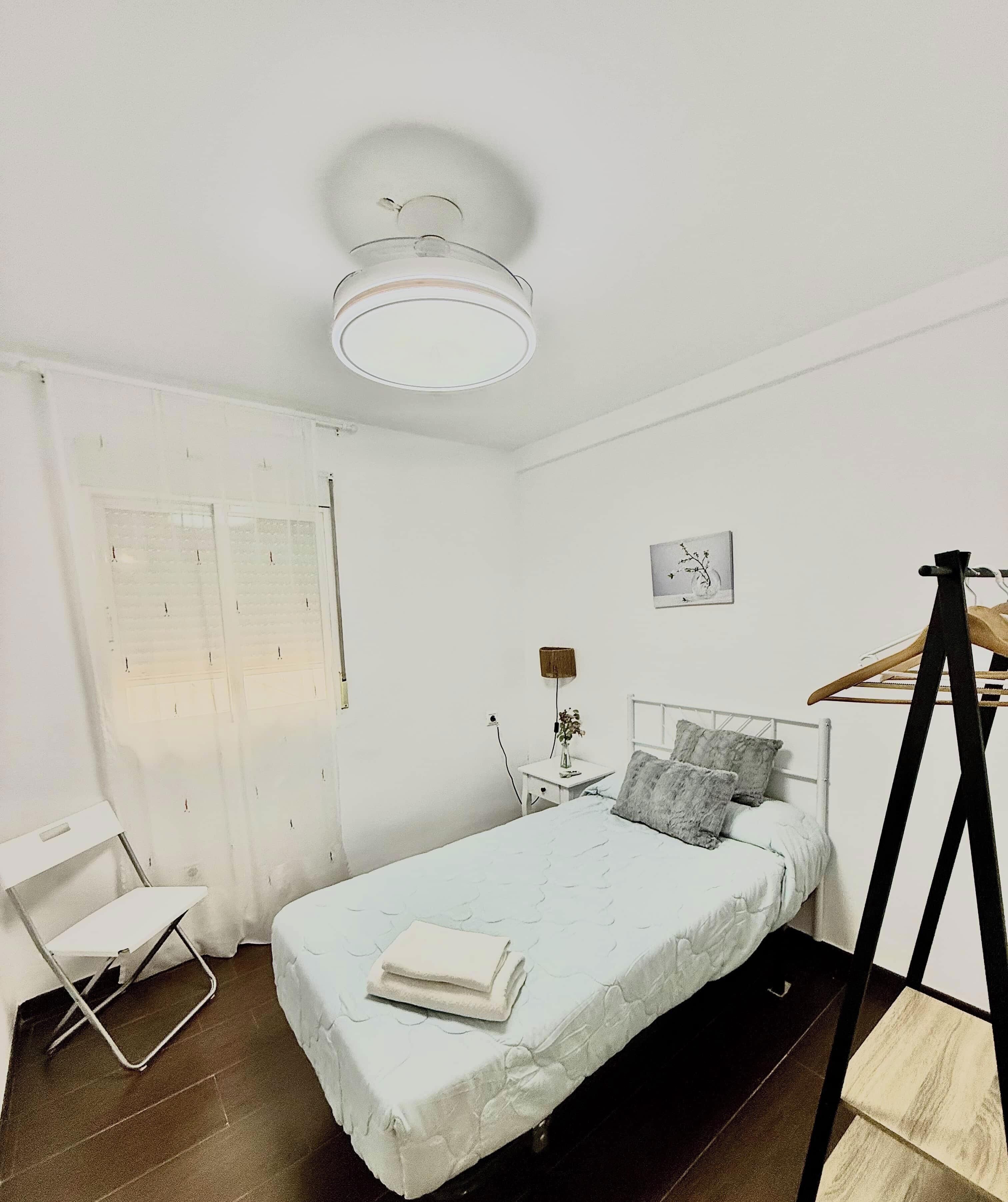 Une chambre à coucher au style minimaliste, avec un lit, une table de chevet, une lampe et un portant à vêtements suspendu.