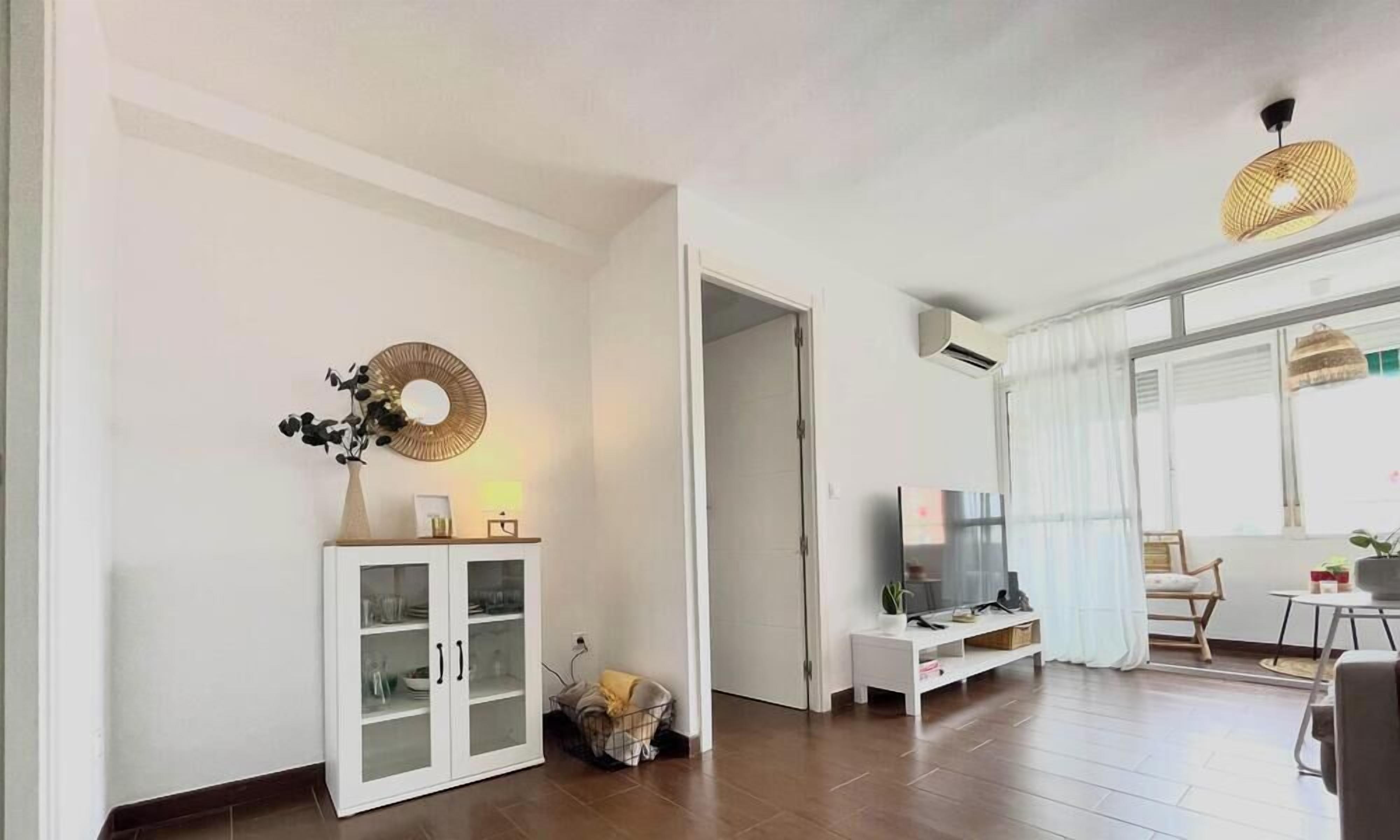 Una sala de estar con un aparador blanco, un televisor y una lámpara de mimbre.