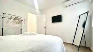 Een slaapkamer met een bed, een aan de muur bevestigde televisie en een kledingrek.