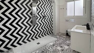 A bathroom with a black and white chevron-patterned wall, a patterned floor, a white sink, and a window.