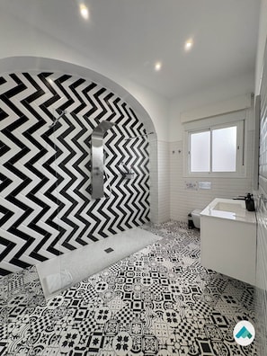 A bathroom with a black and white chevron-patterned wall, a patterned floor, a white sink, and a window. - Rest in the Heart: Córdoba (Córdoba)