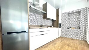 Een moderne keuken met een roestvrijstalen koelkast, witte kasten, een houten aanrechtblad en behang met een patroon.