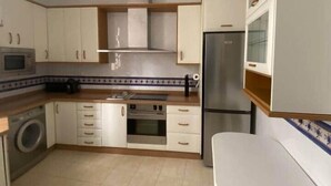 Eine kleine Küche mit weißen Schränken, einem Edelstahlbackofen, einer Mikrowelle und einem Kühlschrank.