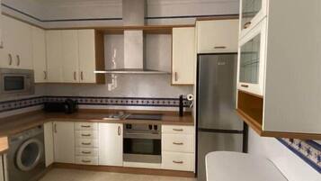 A compact kitchen with white cabinets, a stainless steel oven, a microwave, and a refrigerator.