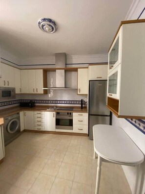 A compact kitchen with white cabinets, a stainless steel oven, a microwave, and a refrigerator. - Home Tendillas de Córdoba (Córdoba)