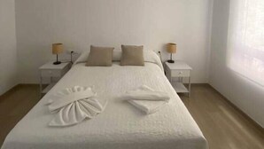 Ein schlichter Schlafzimmer mit einem großen Bett, zwei Nachttischen mit Lampen und einer Pendelleuchte.