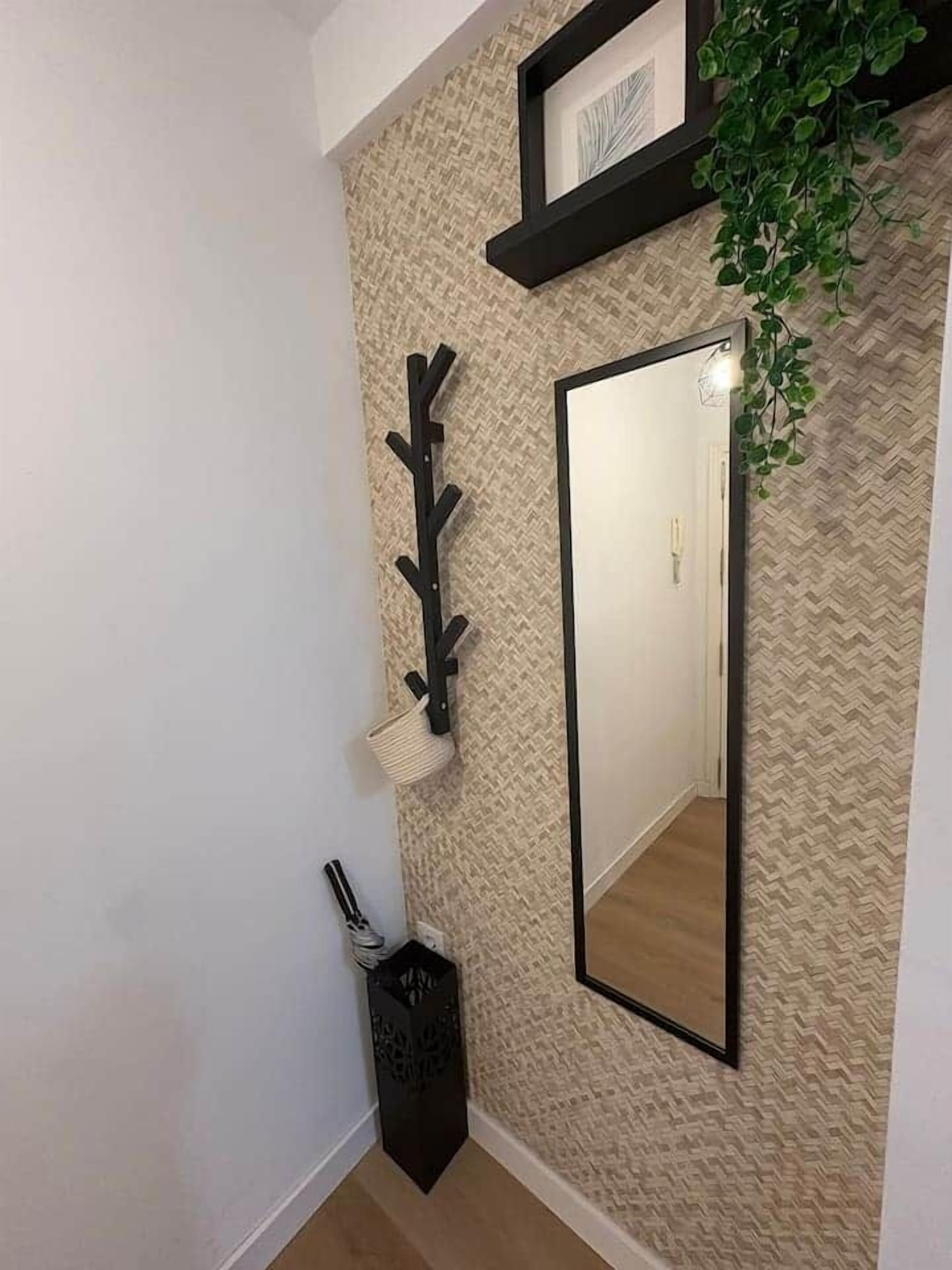 Un couloir avec un mur à texture, un porte-manteau noir, un miroir et une plante en pot.