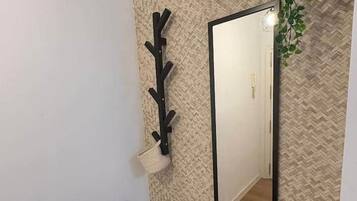 Un couloir avec un mur à texture, un porte-manteau noir, un miroir et une plante en pot.