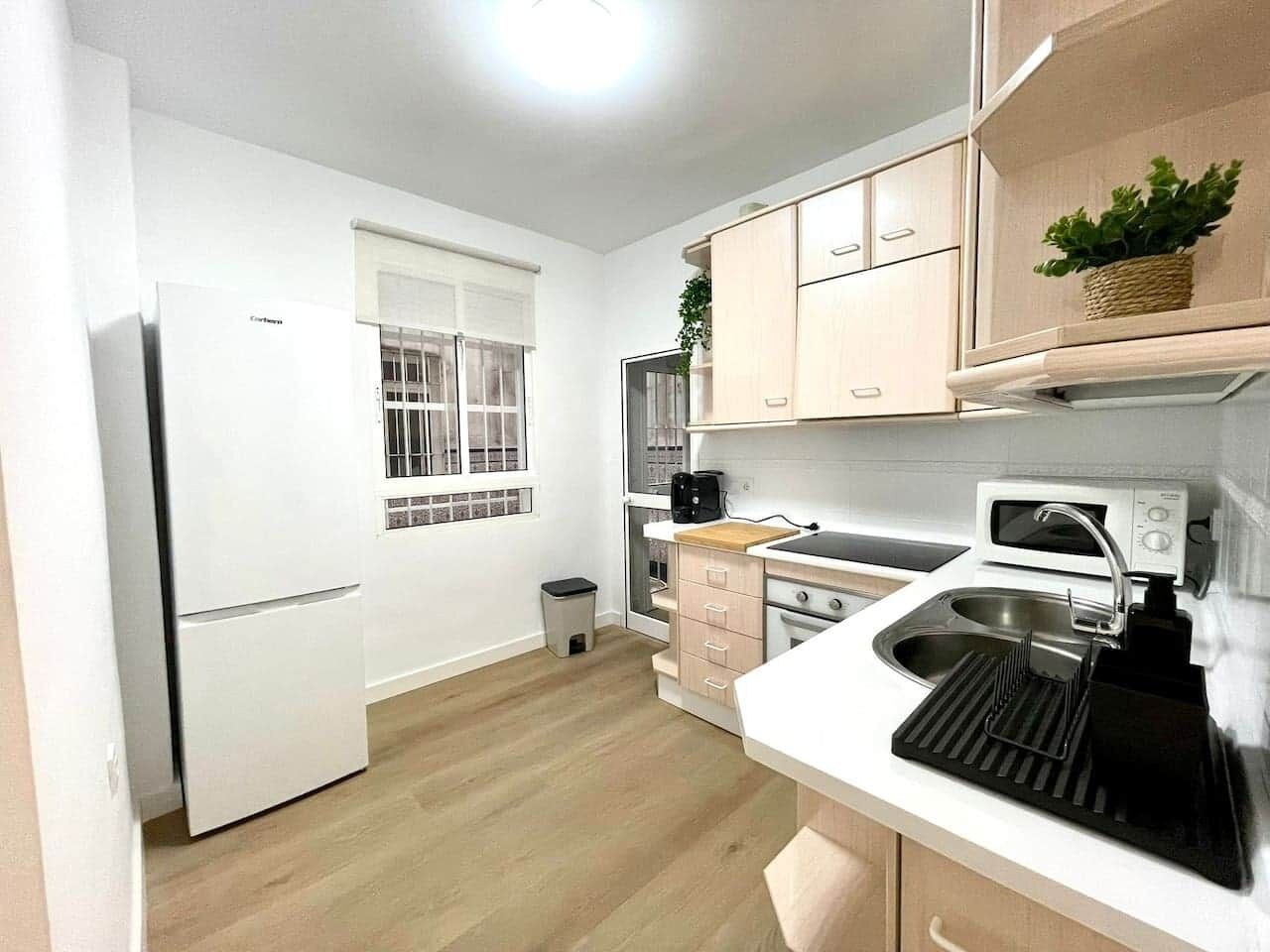 Une cuisine compacte équipée d’un réfrigérateur, d’un four à micro-ondes, d’un évier et de meubles de rangement en bois.