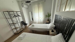 Une chambre d’hôtel avec deux lits, une armoire en métal, une petite table avec une lampe et une plante en pot.