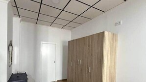 Una habitación con techo de baldosas, un armario, una puerta y una mesita.