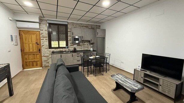Una sala moderna con sofá, mesa de comedor y sillas, una cocina equipada y un mueble para televisor.