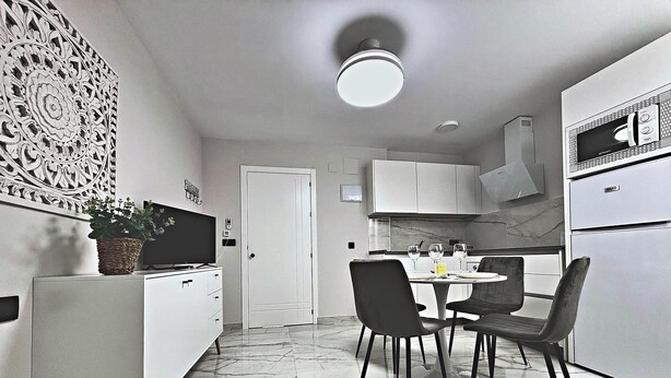 A modern kitchen with white cabinets, a dining table with chairs, a microwave, and a decorative wall piece. - Mirador de Santa Marina Complete (Córdoba)