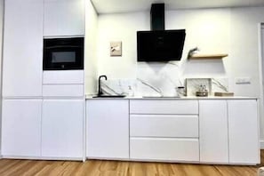 A modern kitchen with white cabinetry, a black microwave, and a small shelf with decorative items. - House in City Garden 1 (Córdoba)